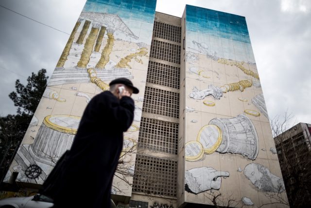 An elderly man talks on his cellphone as he walks past a mural depicting the Greek economy crisis covers a building housing student residences, in Thessaloniki, Greece on March 13, 2015. / Μια τοιχογραφία που απεικονίζει την κρίσης της Ελληνικής οικονομίας καλύπτει ένα κτίριο που στεγάζει φοιτητικές εστίες, στη Θεσσαλονίκη, Ελλάδα στις 13 Μαρτίου, 2015.