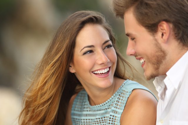 Funny couple laughing with a white perfect smile and looking each other outdoors with unfocused background