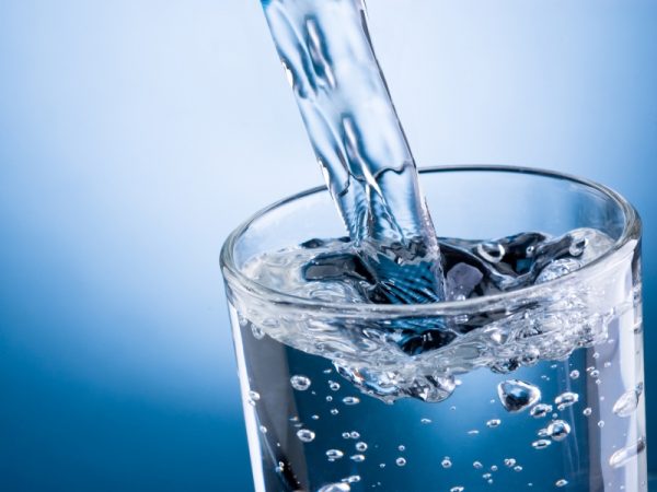 Pouring water into glass on blue background