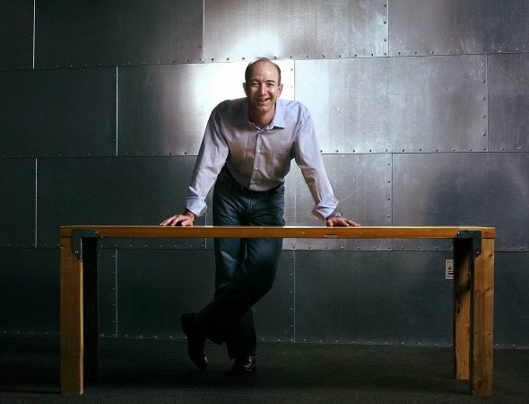 Jeff Bezos, founder, CEO and chairman of Amazon.com, stands with one of the company's trademark door-desks at the company's Seattle headquarters, Thursday, March 11, 2004. A decade after its founding, the Internet retailing giant has experienced more dizzying ups and downs than most companies experience in decades of doing business. Bezos says it's still way too early to say whether Amazon is getting close to a phase that could be called business as usual. (AP Photo/Andy Rogers)