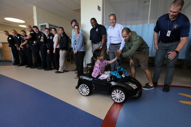 Andrea Destraio, 5, slaps hands with San Diego Harbor police officer Aldo Gutierrez and other officers whose charity donated to Rady Children's Hospital to start a program that uses remote control cars to take young patients to the operating room, in San Diego, California, U.S. September 19, 2017.     REUTERS/Mike Blake