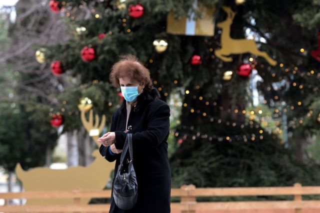 γυναίκα με μάσκα μπροστά στο χριστουγεννιάτικο δέντρο
