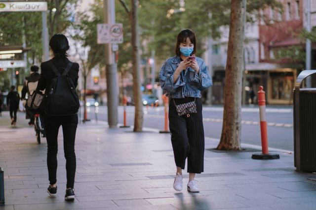 κοπέλα με κινητό και μάσκα στο δρόμο