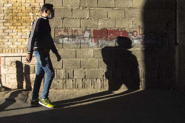 ο άντρας περπατά στο δρόμο με μάσκα και η σκιά του
