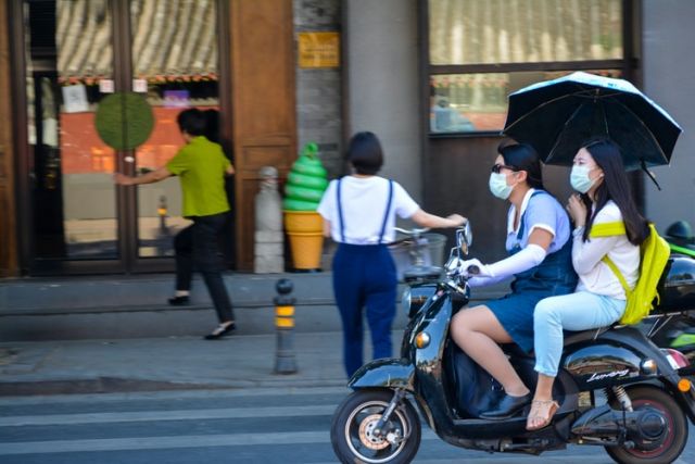 ζευγάρι κινέζων σε μηχανάκι με μάσκα και ομπρέλα