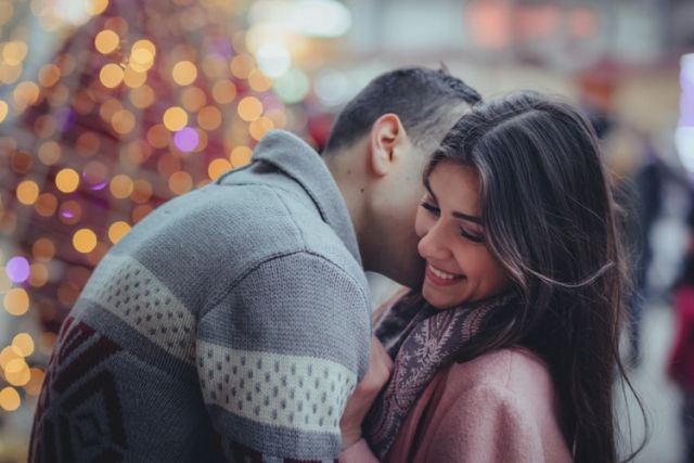 ζευγάρι φιλιέται με φόντο χριστουγεννιάτικα λαμπάκια